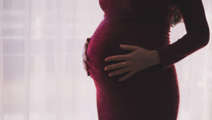 Mulher grávida usa vestido vermelho e coloca a mão na barriga