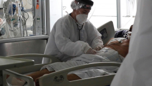 Profissional de saúde vestido a caráter atende paciente com Covi-19 deitado em maca