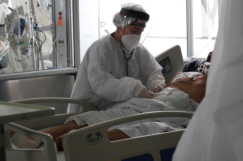 Profissional de saúde vestido a caráter atende paciente com Covi-19 deitado em maca