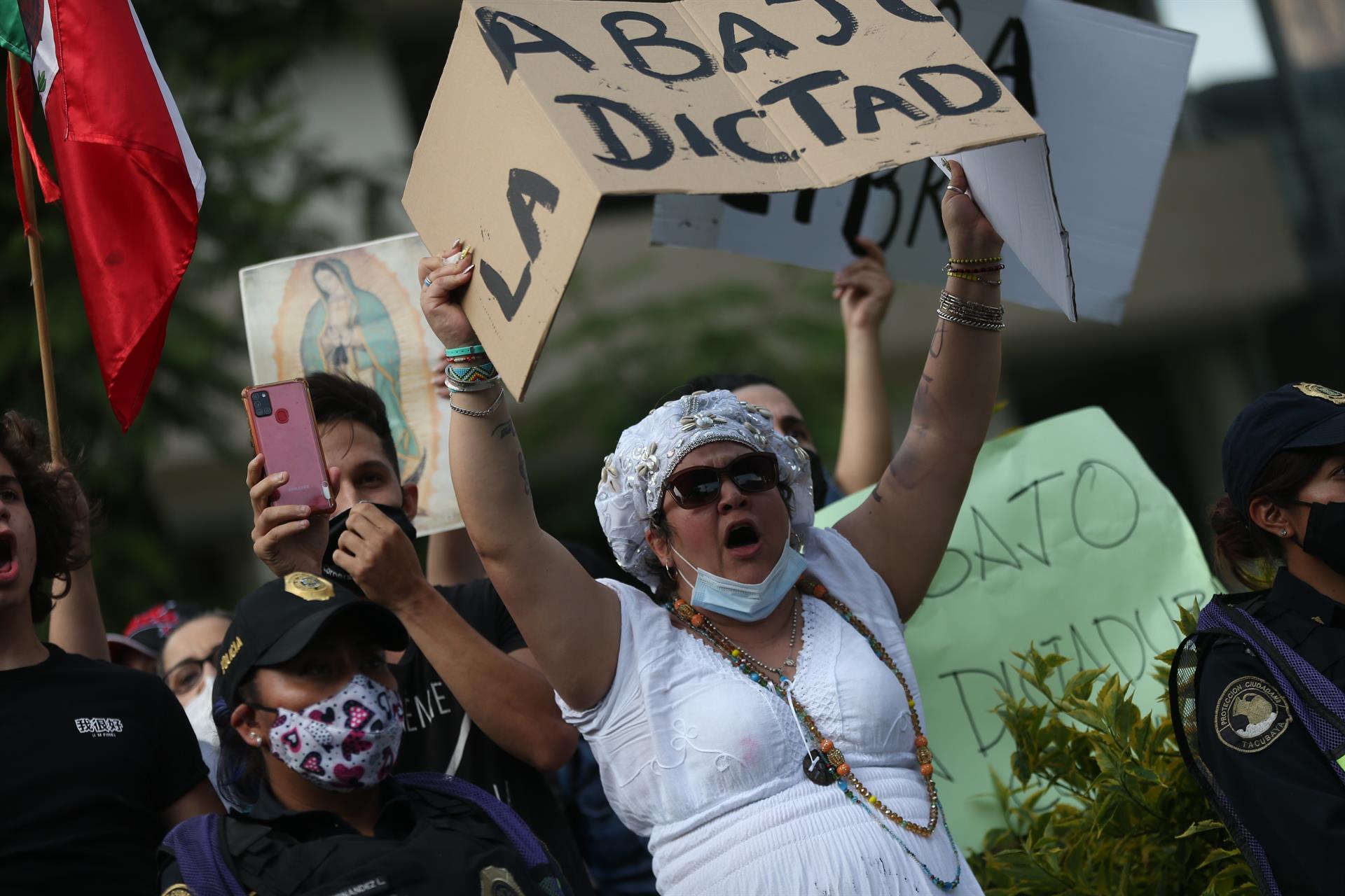 Pessoas protestando, mulher em evidência carregando um papelão escrito 'Abajo la dictadura'