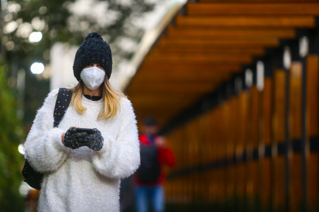 Mulher usa blusa de lã branca, touca e luvas pretas para se proteger contra o frio