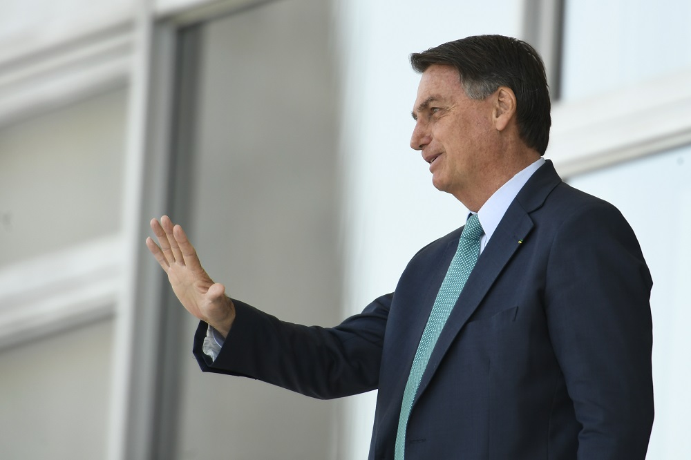 De traje social, o presidente Jair Bolsonaro acena