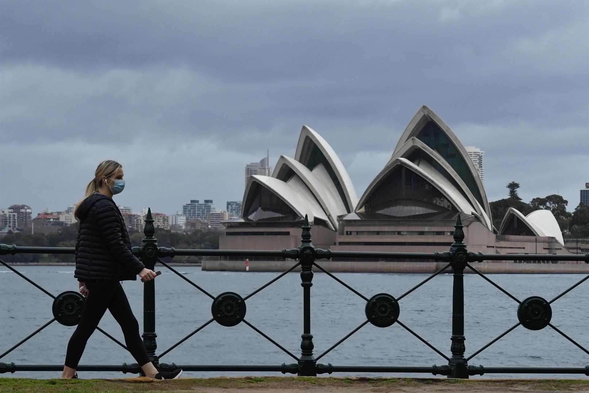 Mulher usando máscara caminha em frente ao monumento Opera House, na Austrália.