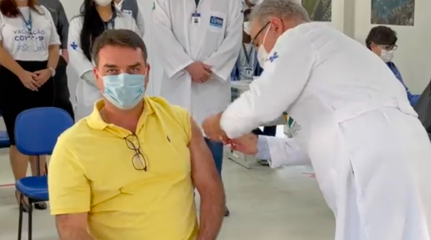O senador Flávio Bolsonaro recebendo a primeira dose da vacina contra a Covid-19 pelo ministro Marcelo Queiroga