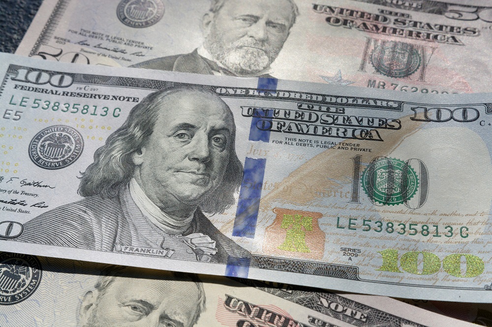 Imagem mostra três notas de dólares, uma de 100 no meio de duas de 50, colocada sobreposta às outras
