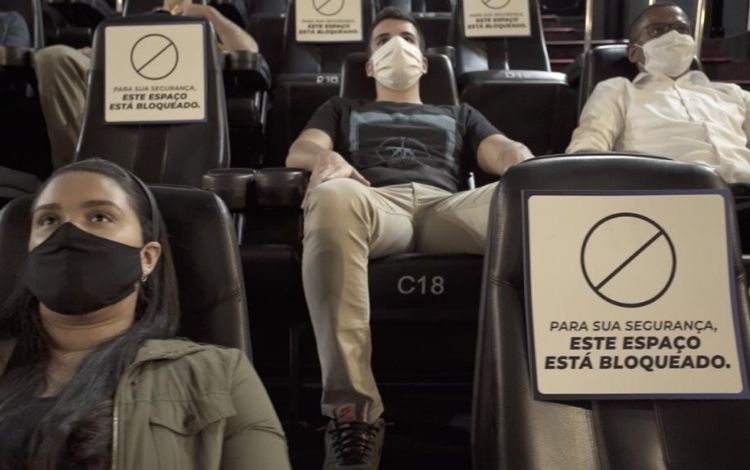 Pessoas em uma sala de cinema usando máscara
