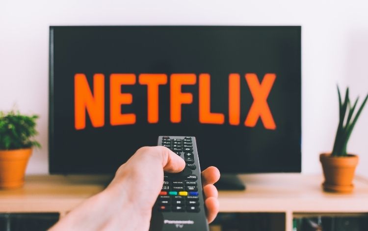 Televisão cMão de uma pessoa usando um controle remoto em frente a uma TV da Netflix
