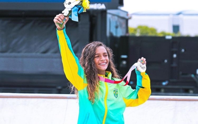 Rayssa Leal levantando um buquê de flores e com a medalha de prata na outra mão