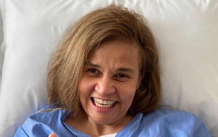 Claudia Rodrigues sorrindo deitada em uma cama de hospital