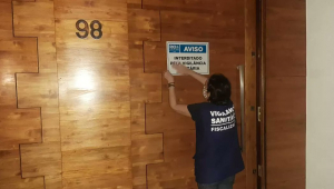 Fiscal da Vigilância Sanitária fixa placa de interditado em porta marrom