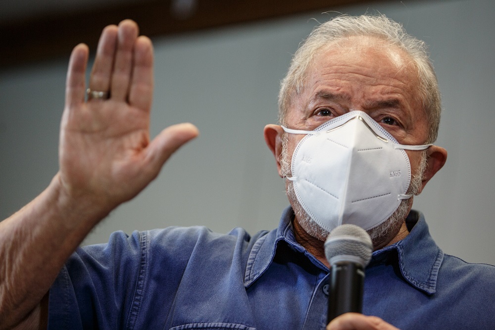 De camisa azul jeans e máscara branca Pff2, Lula ao microfone