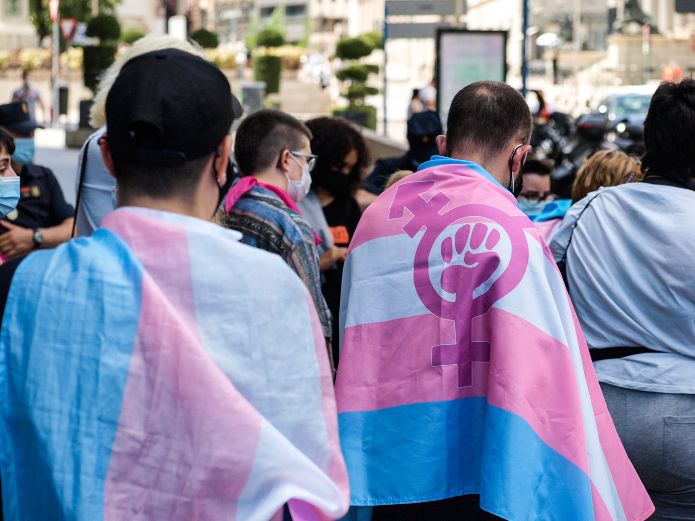 Duas pessoas cobertas por Bandeira do Orgulho Transgênero em uma manifestação na Espanha