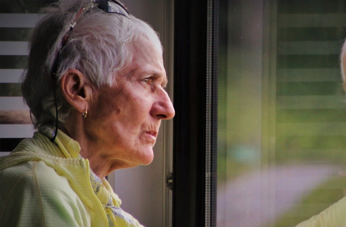 idosa de perfil olhando para fora da janela com olhar pensativo