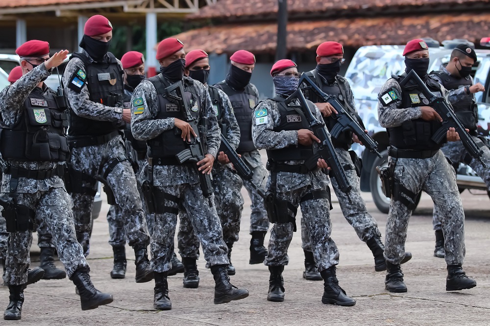 De roupa camuflada, boina vermelha, máscara e fuzil na não, militares da Força de Segurança Nacional caminham por uma rua de Manaus, um perto do outro