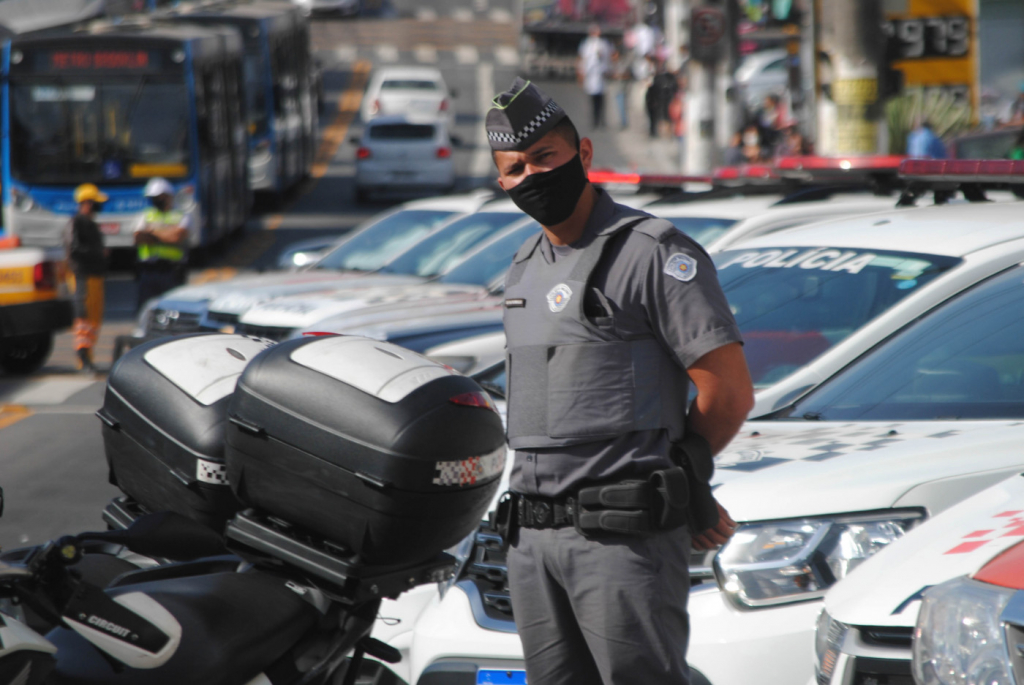 Policial militar usa uniforme da corporação e máscara de proteção preta