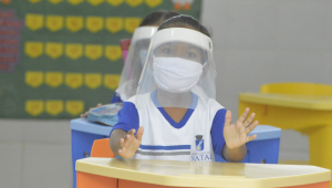 Aluna usa máscara de proteção e face shield dentro de sala de aula