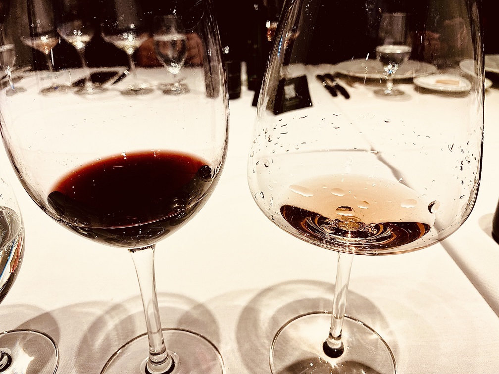 Duas taças de vinho pouco cheias, uma com vinho tinto outra com vinho branco em cima de uma toalha de mesa branca