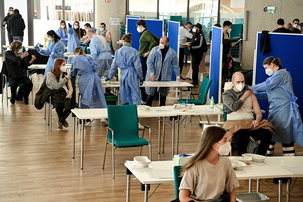 Posto de vacinação em Berlim com profissionais de saúde usando avental azul e algumas pessoas tomando vacina