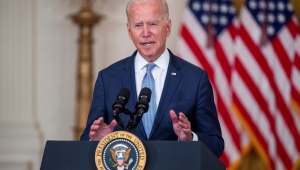 Joe Biden falando em microfone diante de bandeiras dos Estados Unidos