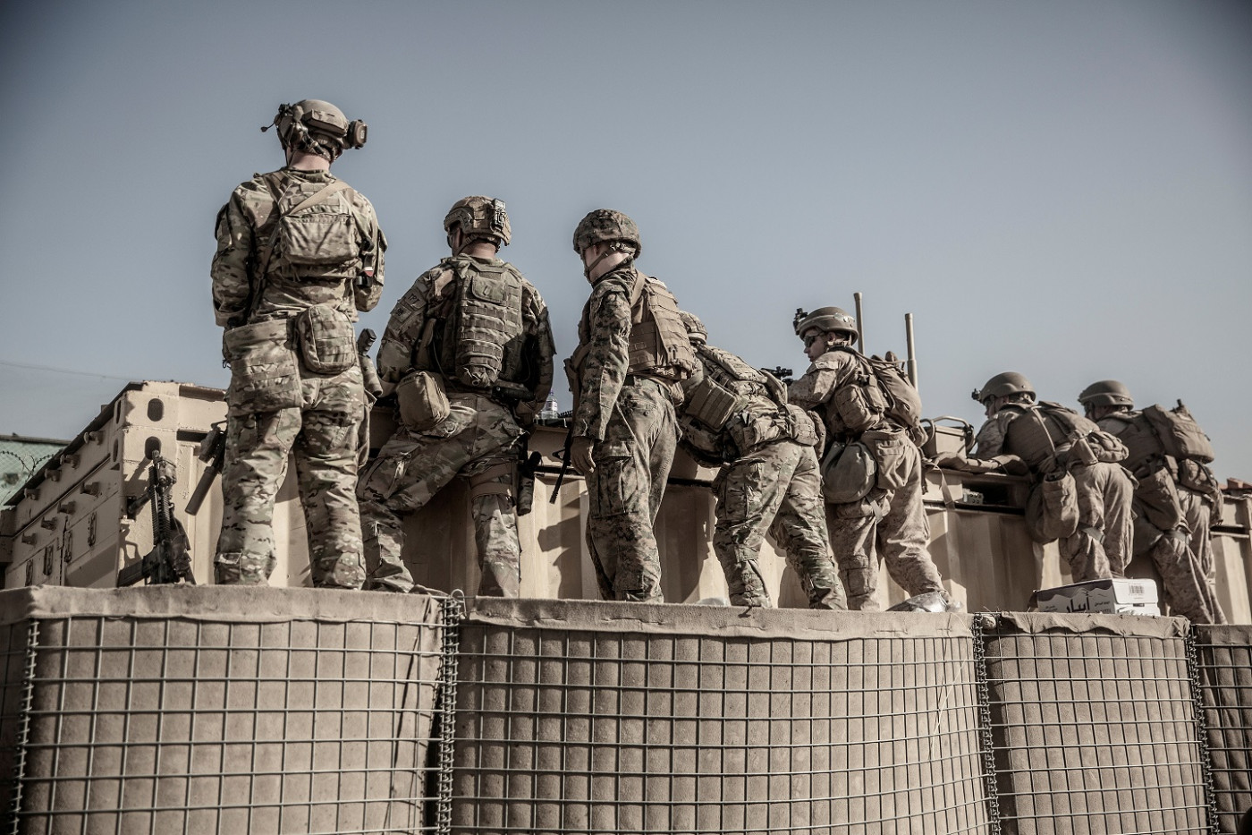 Um grupo de soldados com uniformes militares lado a lado de costas em cima de uma espécie de muro