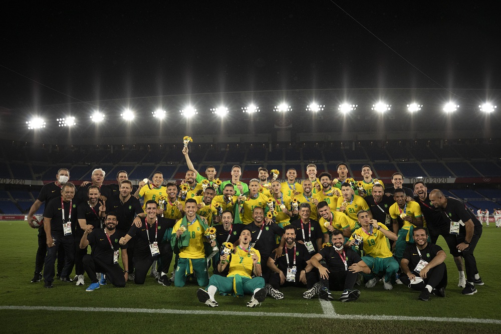 Jogadores da seleção brasileira se amontoam, com alguns agachados e outros em pé, em foto posada após o título olímpico