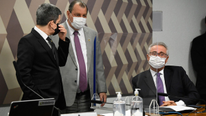Randolfe Rodrigues e Omar conversam em pé (e usando máscaras) durante sessão da CPI, enquanto Renan Calheiros ouve a conversa do aliados sentado em seu lugar