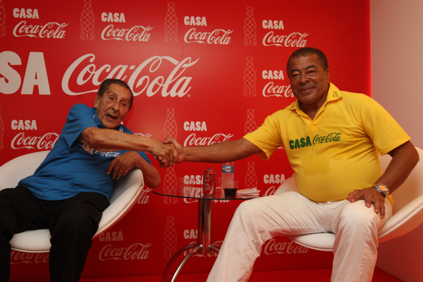 Dois homens idosos dando as mãos, um com a camiseta do Brasil e outro de camiseta azul