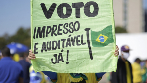 Pessoa segura uma placa escrito "voto impresso e auditável já' com uma bandeira do brasil desenhada
