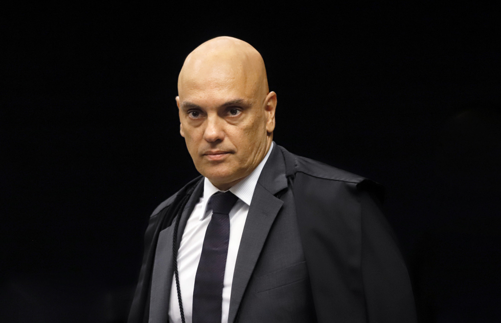 Ministro Alexandre de Moraes usando terno com fundo preto. Olha para a câmera, está de terno preto e camisa branca. Ele é careca