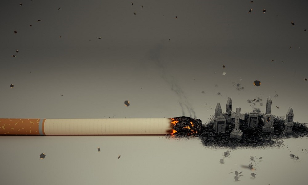 Fotomontagem com um cigarro queimando em cima de uma superfície, e as cinzas se arrastam para um pequeno cemitério