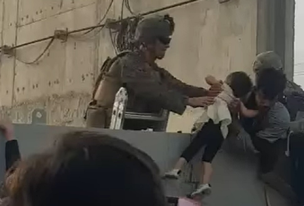 Criança sendo passada por cima de muro no aeroporto de cabul