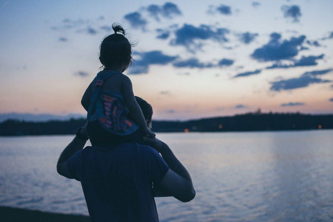 Homem com criança nos ombros de costas olhando para um rio