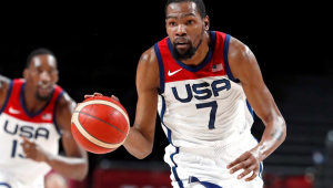 Com uniforme branco da seleção americana de basquete, o jogador Kevin Durant (de bigode e cavanhaque) maneja a bola antes de batê-la no chão