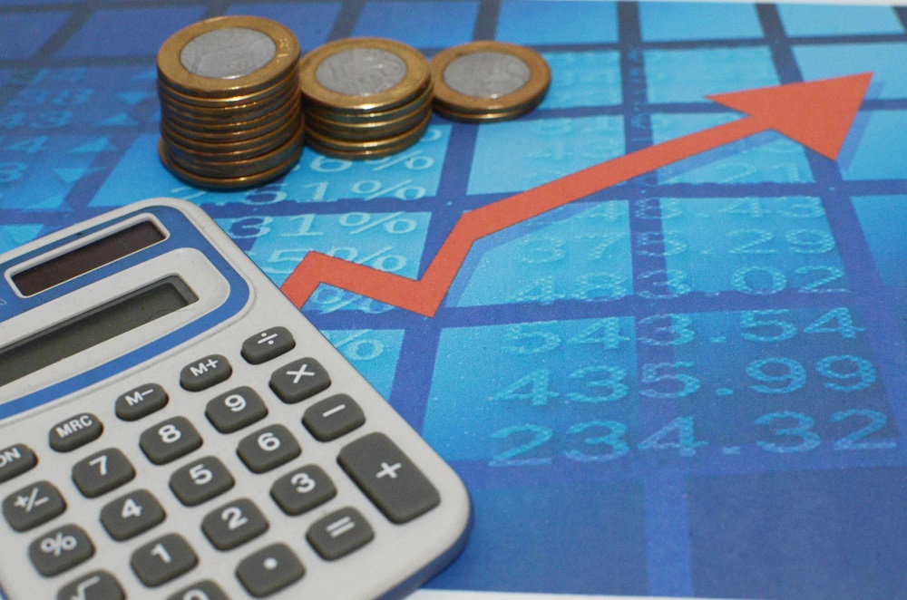 Imagem com uma calculadora, uma seta para cima e moedas representa o aumento da inflação