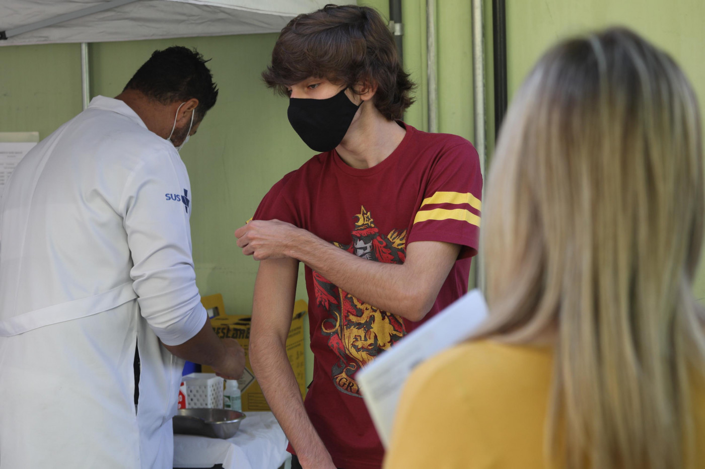 Adolescente arregaçando as mangas da blusa para receber a vacina contra a Covid-19
