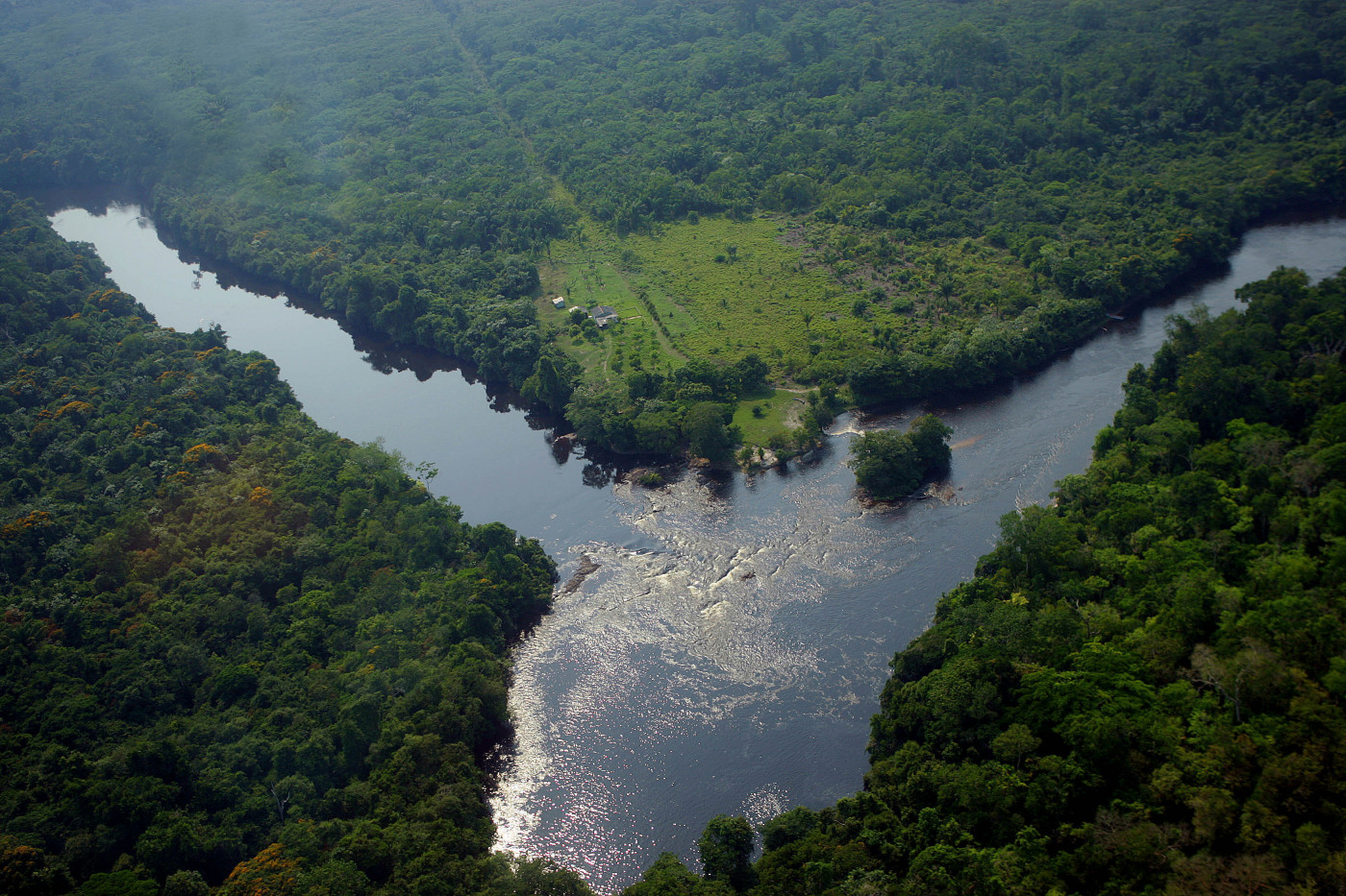 Foto tirada de cima de duas nascentes de um rio que se encontram no meio, onde ele fica mais cheio. Em volta, uma floresta com bastante vegetação