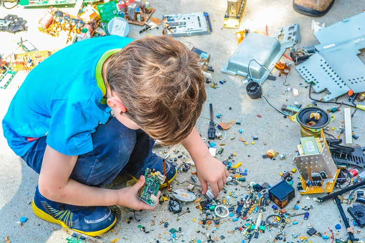 Criança brincando com vários pedaços de um objeto tecnológico espalhados pelo chão