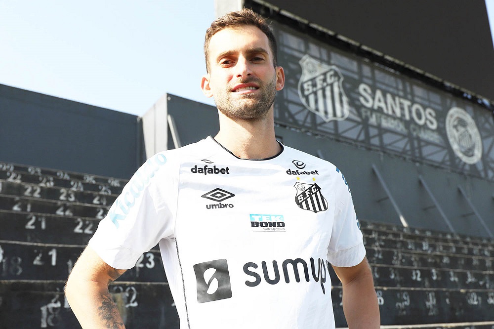 Léo Baptistão posa para foto com a camisa do Santos, com a arquibancada atrás