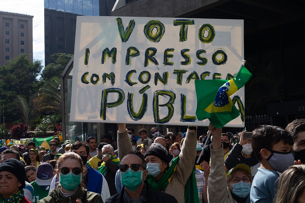 Apoiadores de Jair Bolsonaro, a maioria usando roupa verde-amarela e máscara, amontoa-se perto do Masp; um grande cartaz com a mensagem 