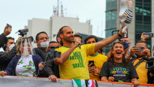 Filho de Bolsonaro, Eduardo Bolsonaro sorrindo com microfone na mão e rodeado de apoiadores em cima de carro de som