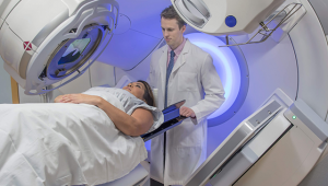 Mulher entrando no aparelho de radioterapia com o auxílio de um médico