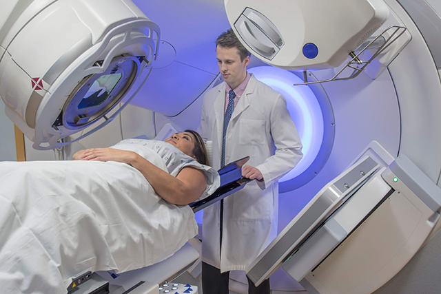Mulher entrando no aparelho de radioterapia com o auxílio de um médico