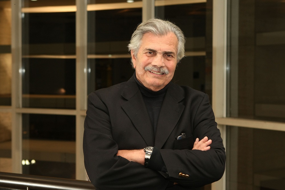 De braços cruzados, usando camisa e blazer preto, o ator Tarcísio Meira posa para um foto em sua casa