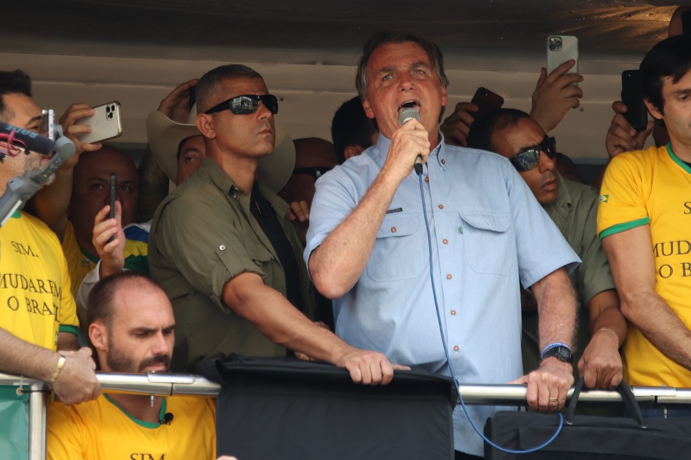 Ao lado de aliados, o presidente Jair Bolsonaro discursa do alto de carro de som na Avenida Paulista, com o microfone em punho e usando uma camisa azul clara