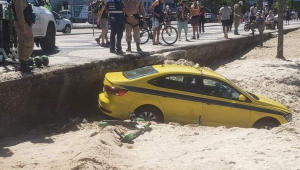 Táxi afundado na areia enquanto pedestres e policiais observam