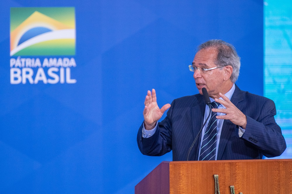 O ministro da Economia, Paulo Guedes, fala à frente de um púlpito com a frase Pátria Amada Brasil atrás dele, na parede azul