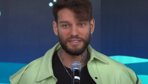 Lucas Lucco usa jaqueta verde e fala no microfone no estúdio do programa Pânico