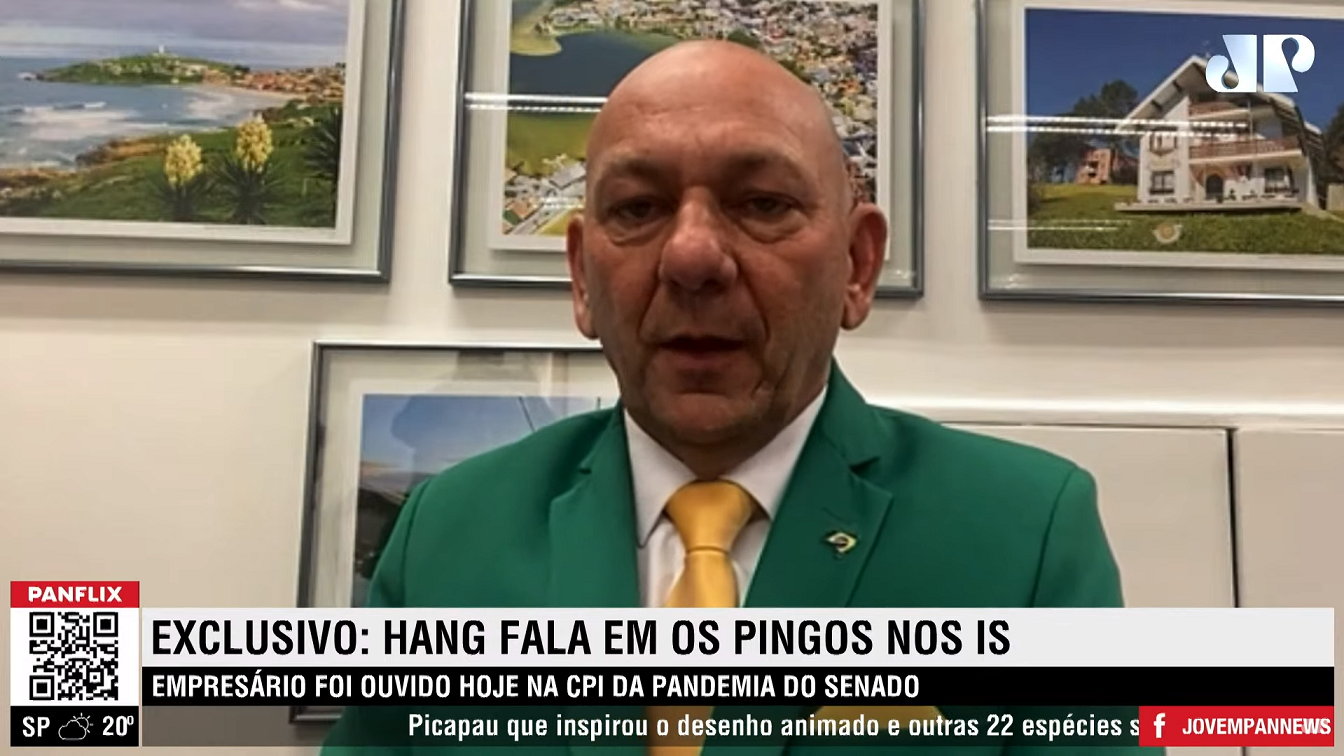 Luciano Hang olhando para a câmera durante participação no programa 'Os Pingos nos Is'. Usa terno verde e gravata amarela