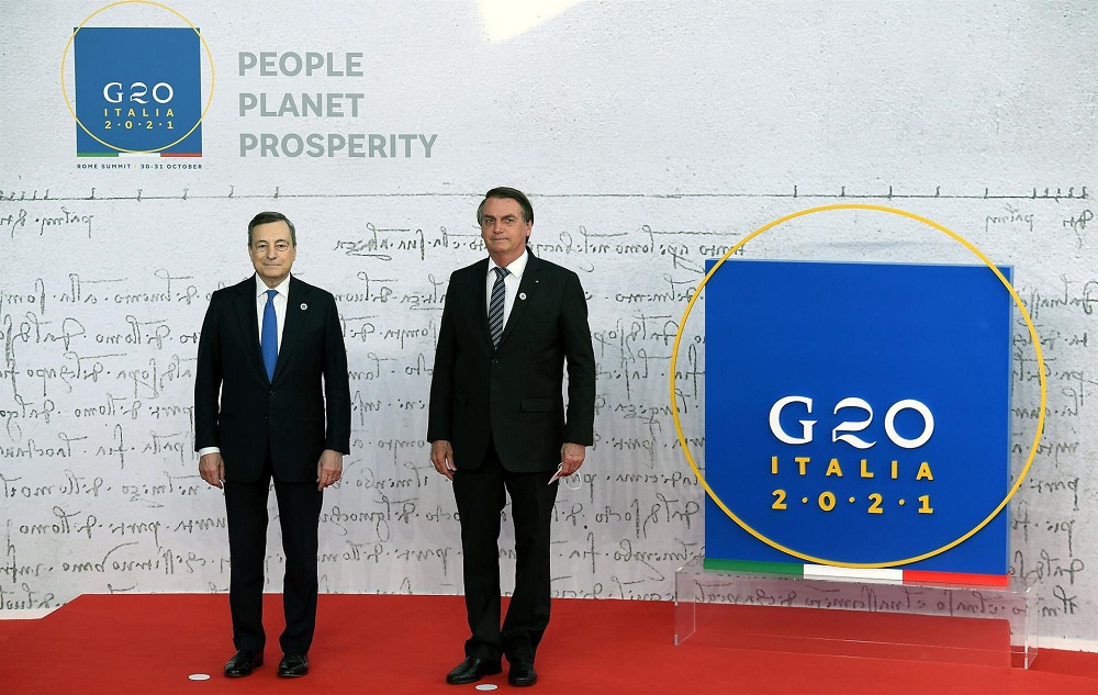 Lado a lado, ambos com trajes sociais, Mario Draghi e Jair Bolsonaro posam para foto em frente a um painel do G20