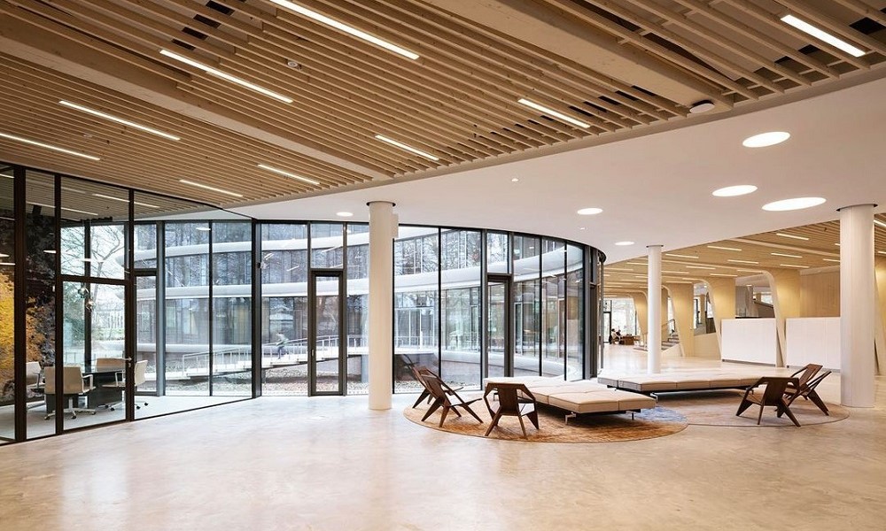 Interior do banco Triodo com um amplo espaço aberto, espreguiçadeiras e cadeiras, num ambiente de cores claras, que transmitem calma, e uma sala de reunião adjacente do lado esquerdo